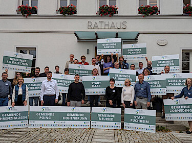 Gruppenbild vor dem Rathaus, die Teilnehmenden stehen hinter Schildern mit den Namen ihrer Kommunen Gruppenbild vor dem Rathaus, die Teilnehmenden stehen hinter Schildern mit den Namen ihrer Kommunen